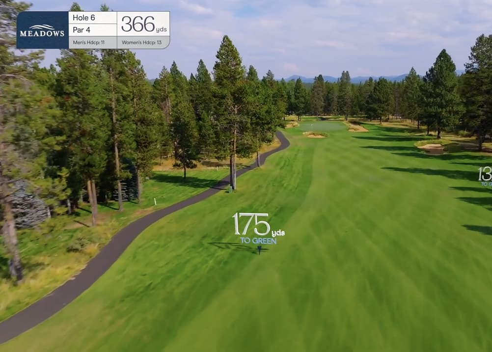 Aerial fairway view of Meadows Golf Course Hole 6, a 366-yard par 4 with a tree-lined hole, cart path on the left, and bunkers guarding the green in the distance.