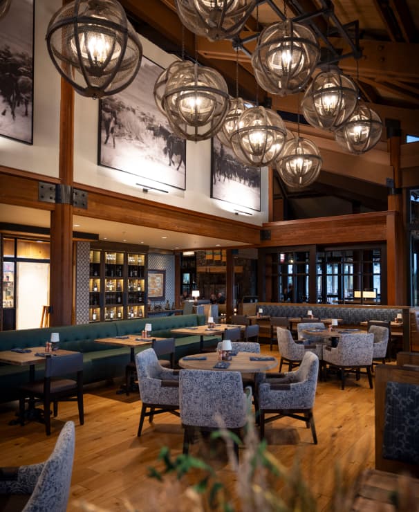 A modern restaurant with wooden floors, round tables, patterned chairs, large hanging globe lights, and black-and-white wildlife photos on the walls. The space looks warm and inviting.