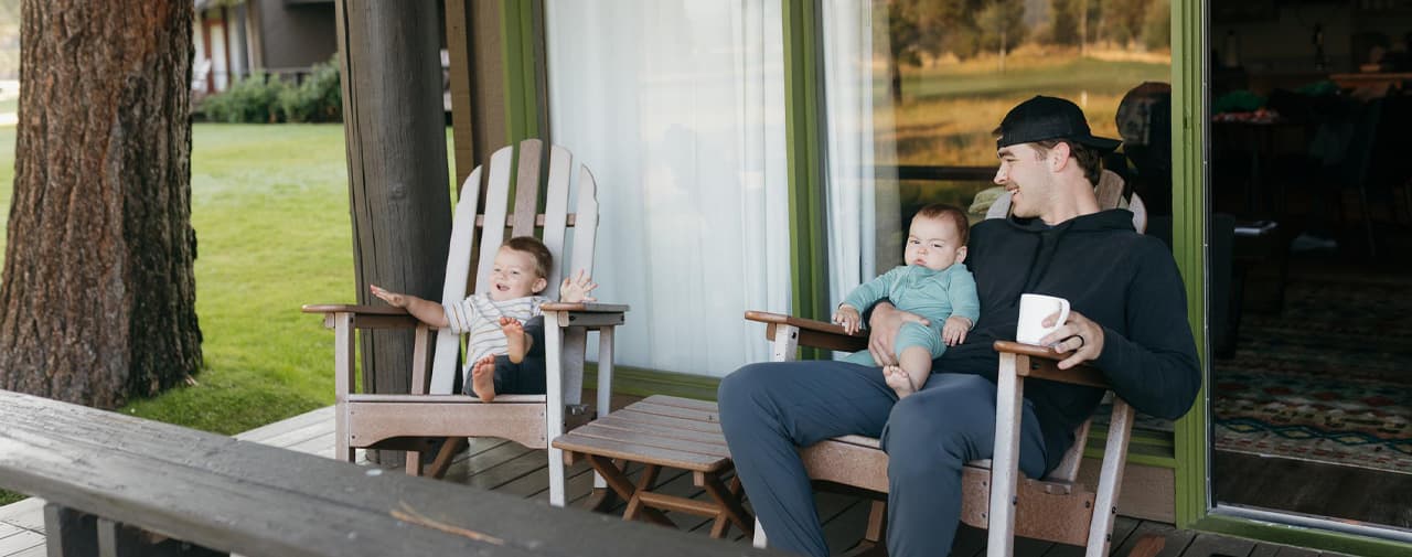 a man and kids sitting on a porch outside, cup of coffee, wooden rocking chairs