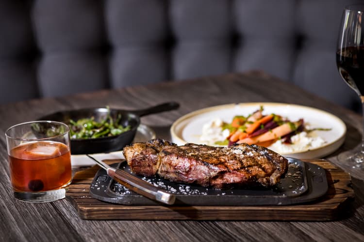 and old fashioned drink, a steak, and assorted vegetables plated on a table