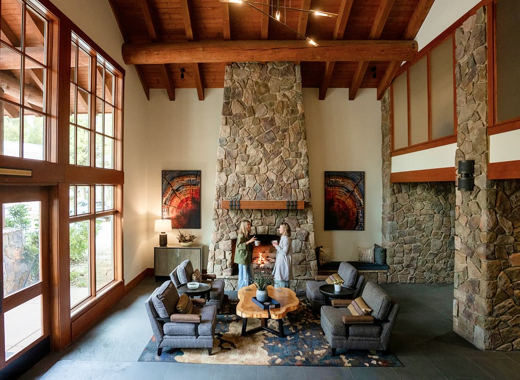 Spacious spa lobby with vaulted wood ceilings, a large stone fireplace, comfortable seating, and guests enjoying the lounge.