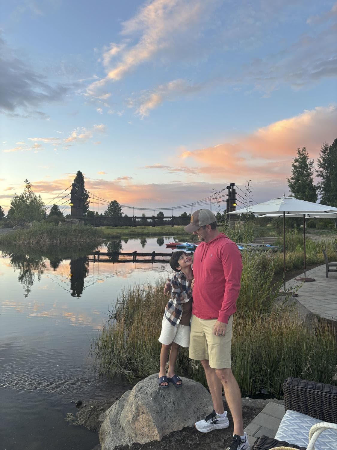 father and son standing on a rock overlooking a lake at sunset