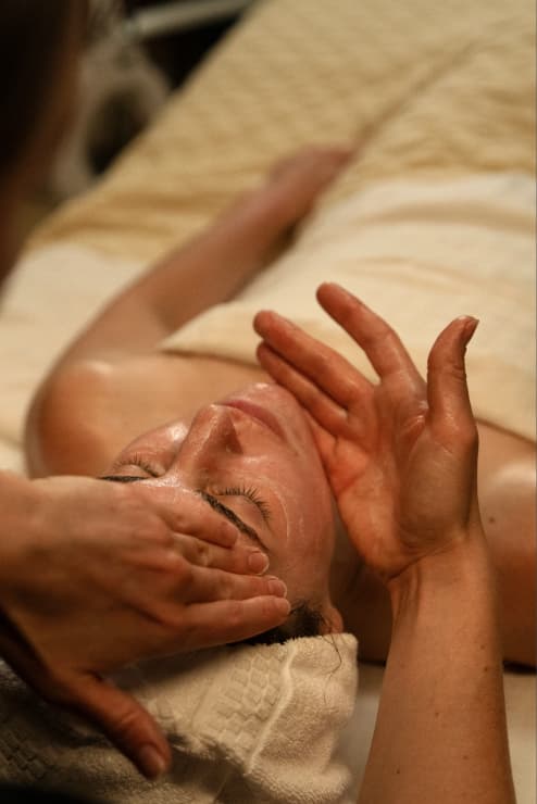 Esthetician performing a relaxing facial treatment on a guest lying comfortably on a spa bed.