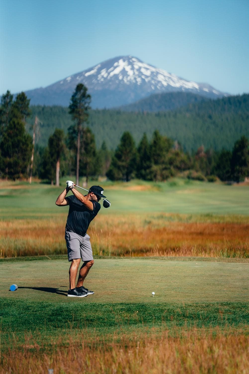 a person hitting a golf ball on Crosswater golf course with Mt. bachelor in the background and blue sky