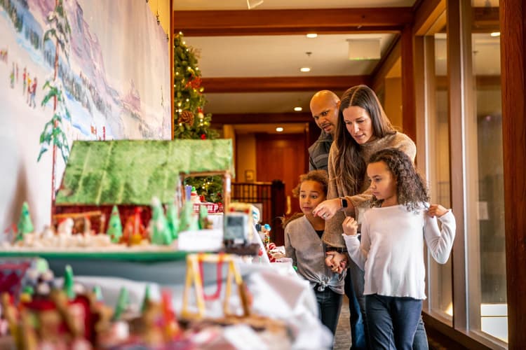 family walking down hallway looking at ginerbread houses displayed on table